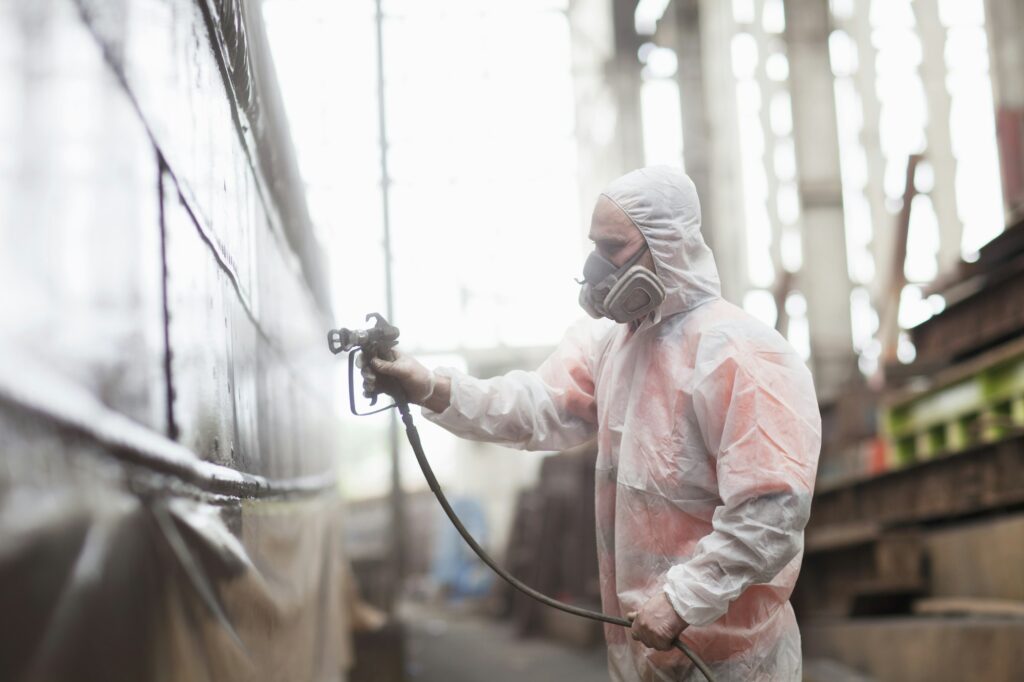 Worker spray-painting boat in shipyard